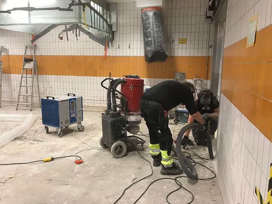 En byggarbetare slipar ett betonggolv med en OxySan bredvid sig